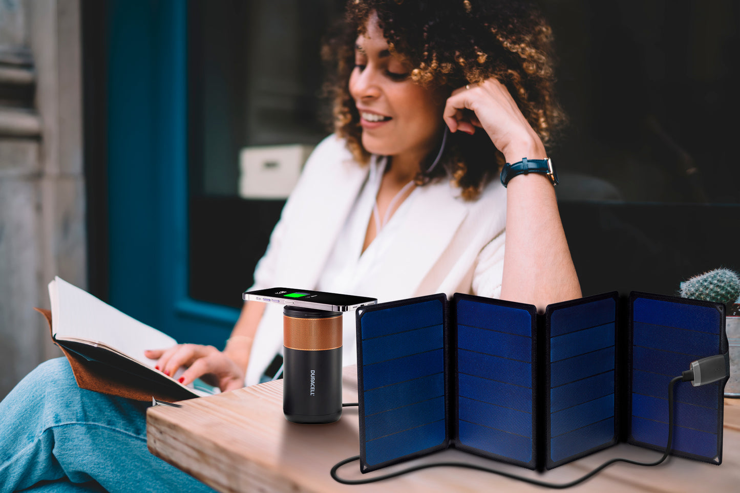 A foldable solar panel powering a charger that powers a phone while a woman works outside